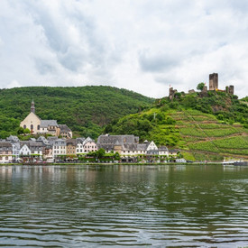 Ein kleines Dorf liegt an einem Fluss und im Hintergrund auf einem Hügel liegt die Burg Beilstein