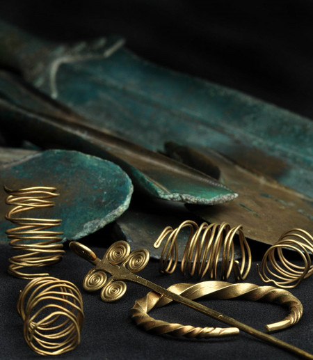 Goldene Spiralen und Gewandnadel, im Hintergrund Beilklingen und ein Kurzschwert