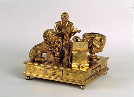 Kleine goldene Figur: kniender Mann vor einem Pult, daneben ein Löwe und ein Fass